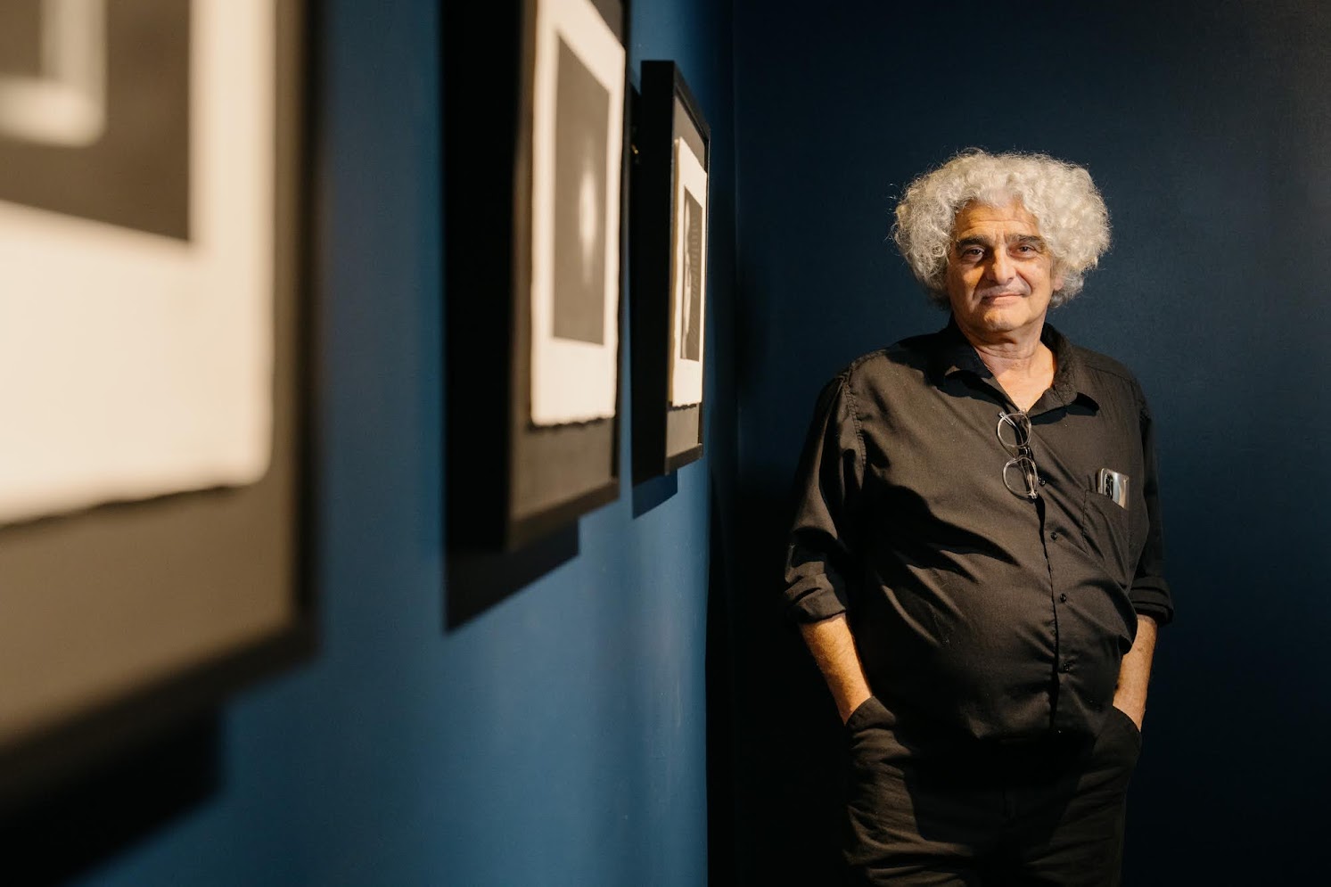 Pantelis Roussakis, printmaker and artist, standing in gallery with framed artwork